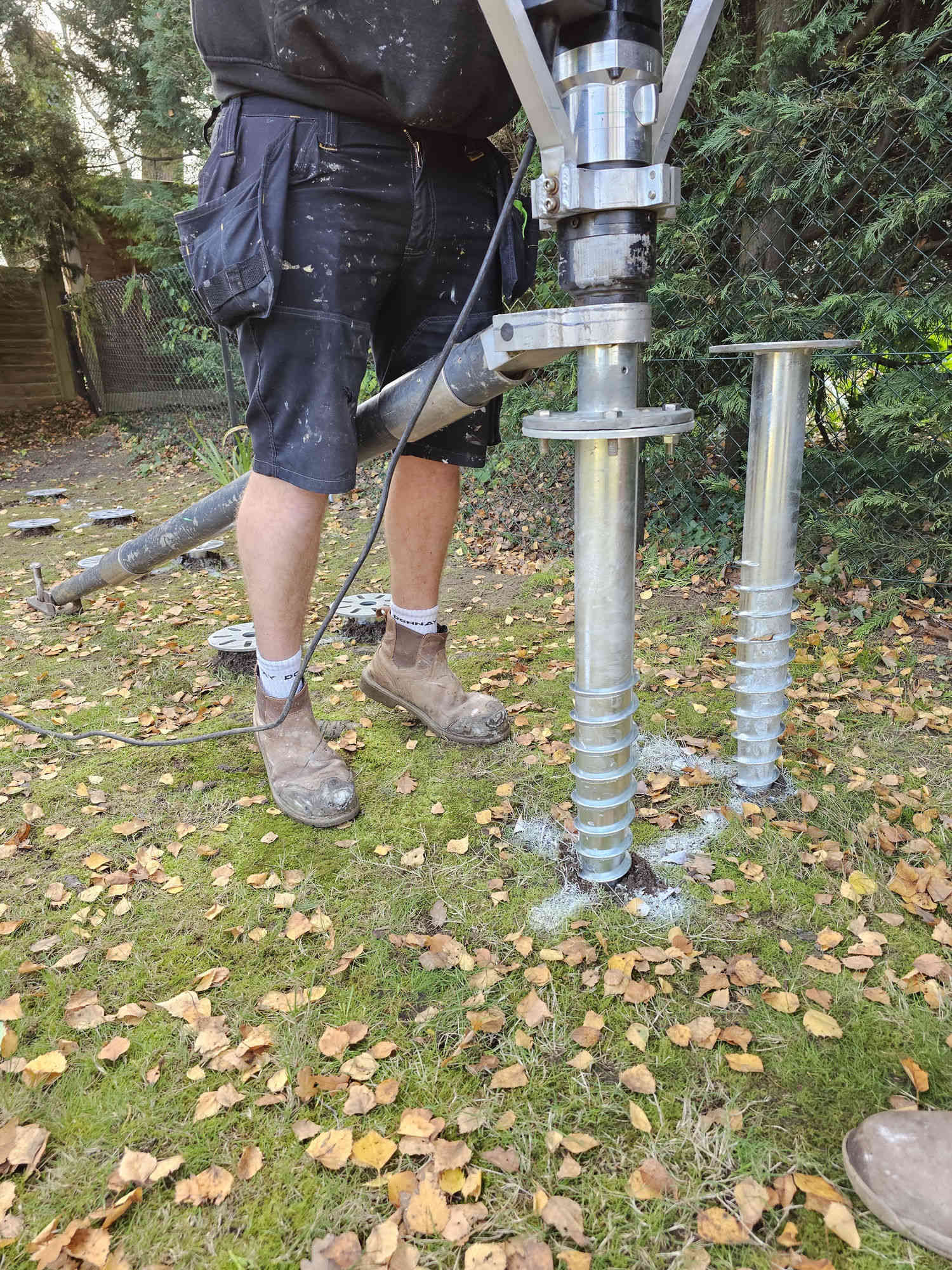 Close-up of an installer driving a ground screw into position, with completed screws visible in the background
